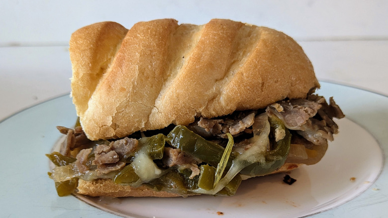 Caramelized onions and green peppers are mixed in with shredded cuts of steak on top of a toasted white sub hoagie roll on a blue and white plate