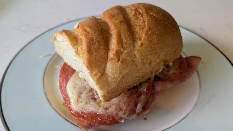 A blue and white plate is topped with a toasted white sub hoagie roll topped with ingredients including pepperoni and cheese and ham.