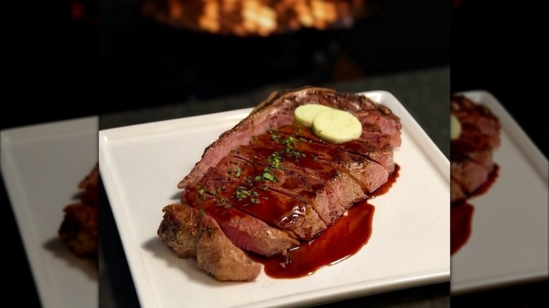 Steak on plate with melting butter and fire blurred in background