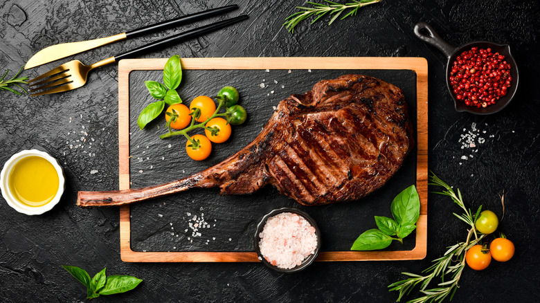 Tomahawk ribeye on board with tomatoes, basil, rosemary, and salt