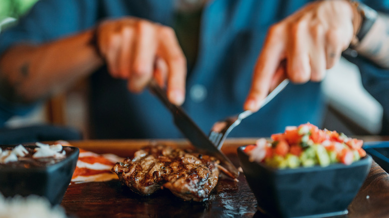 Hands holding a knife and fork and cutting steak