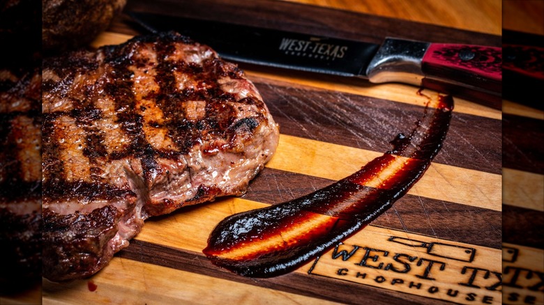 Steak on wooden board with West Texas Chophouse logo and knife