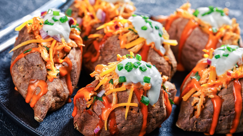 A plate of baked potatoes toped with buffalo chicken, sour cream, and chives.