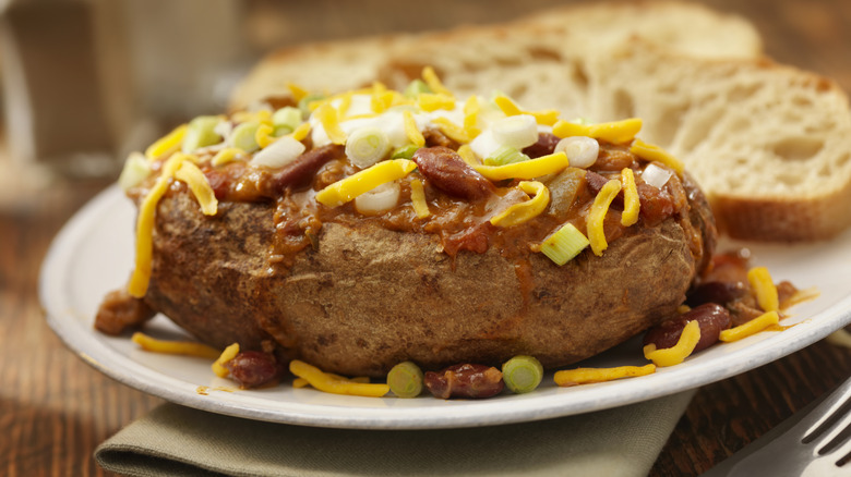 A baked potato topped with chili, sour cream, scallions, and shredded cheese.