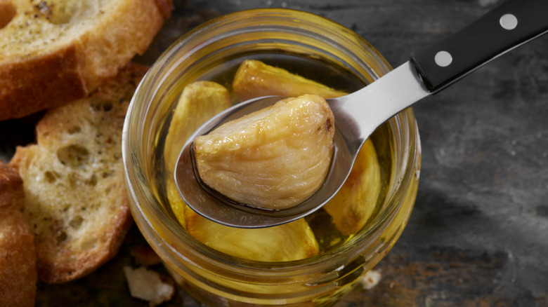 A jar of garlic confit with a spoon and crusty bread.