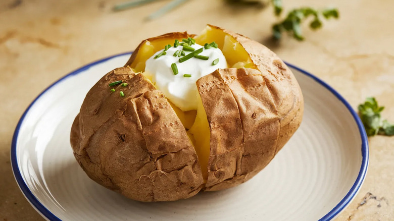 A baked potato on a plate, topped with sour cream and chives.