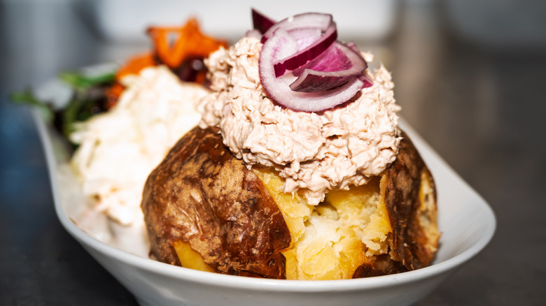 A baked potato topped with tuna salad and sliced red onion.
