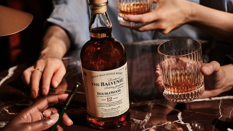 The Balvenie DoubleWood 12-year placed on a table with drinkers holding glasses around it