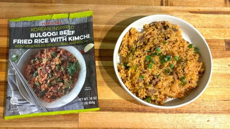 Bag of Trader Joe's Korean-Inspired Bulgogi Beef Fried Rice with Kimchi next to bowl of kimchi fried rice on wooden surface