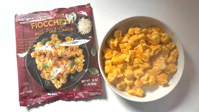 Bag of Trader Joe's Fiocchetti with pink sauce next to bowl of pasta on white surface