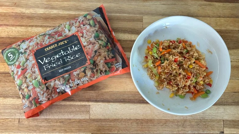 Bag of Trader Joe's Vegetable Fried Rice next to vegetable fried rice in bowl on wooden surface