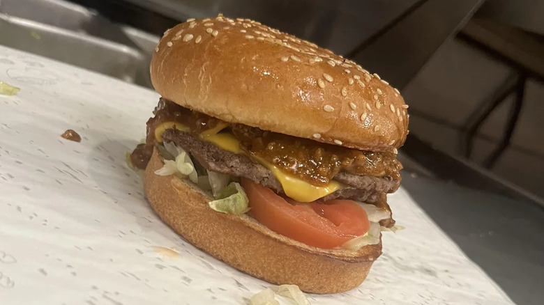 A Del Taco cheeseburger on a sesame seed bun sitting on paper