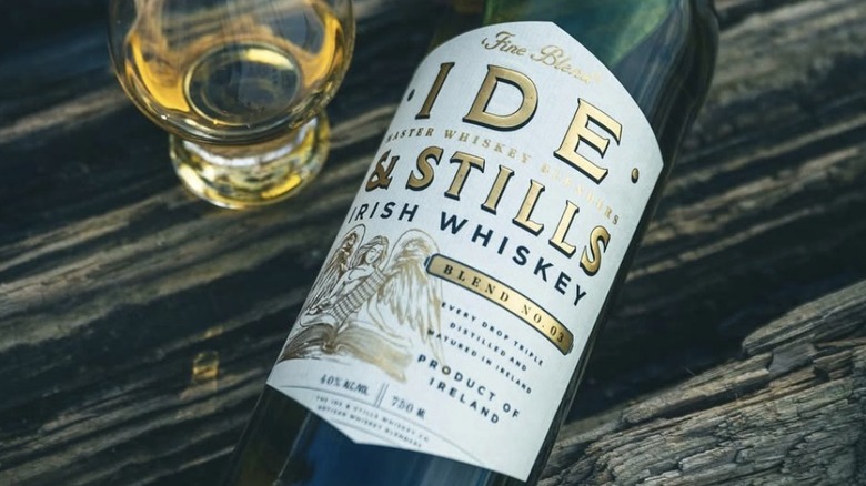 A bottle of Ide & Stills Irish Whiskey laid on a table next to a glass of whiskey