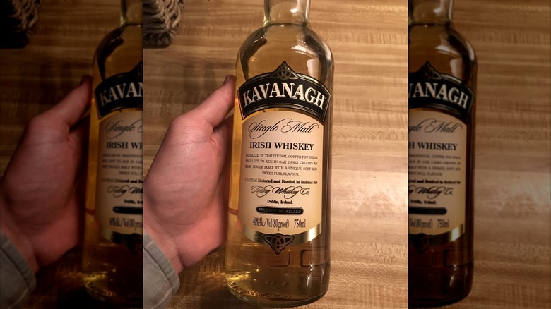 A overhead shot of a person holding a bottle of Kavanagh Irish Whiskey over a wooden table