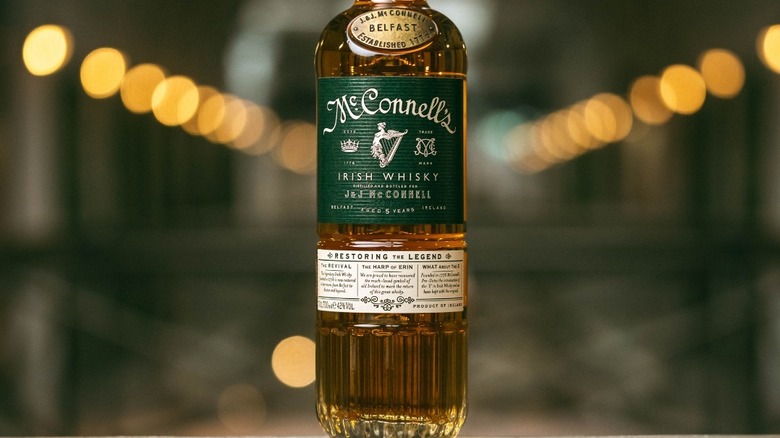 A bottle of McConnell's whisky in the centre of the shot with a blurred lit background