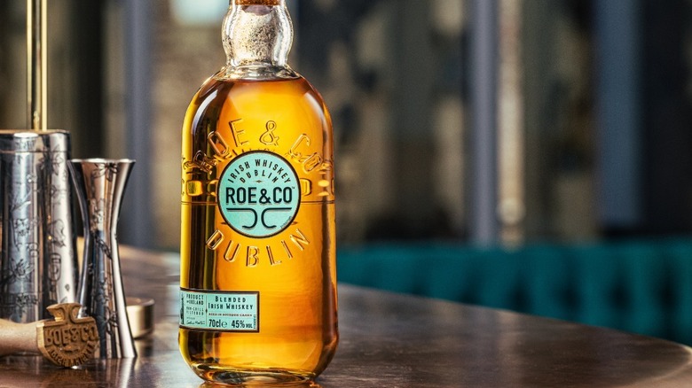 A bottle of Roe & Co posed on the side of a bar next to come cocktail accessories