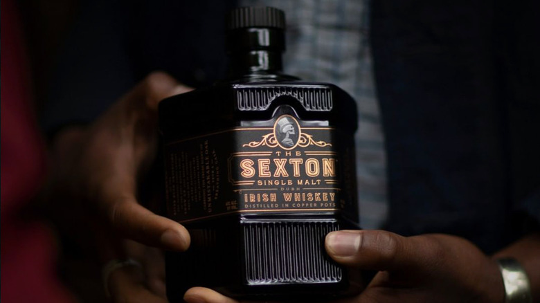 A person holding a bottle of The Sexton up to the camera, showcasing its unique bottle