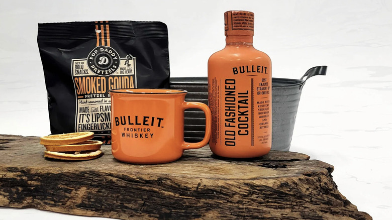 Bulleit's ready-made cocktail next to ceramic mug, orange slices and ceramic mug