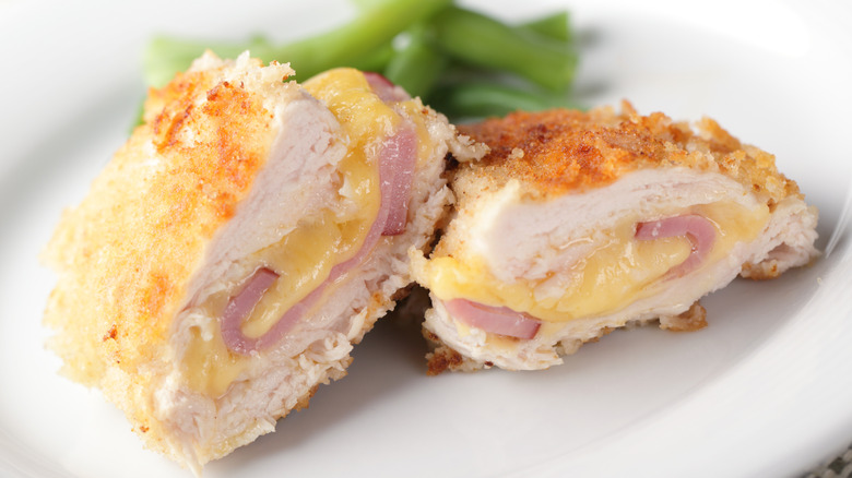 Chicken cordon bleu cut in half served with green beans on a white plate