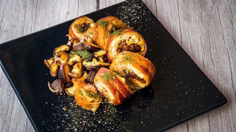Chicken roulade and mushrooms served on a black plate