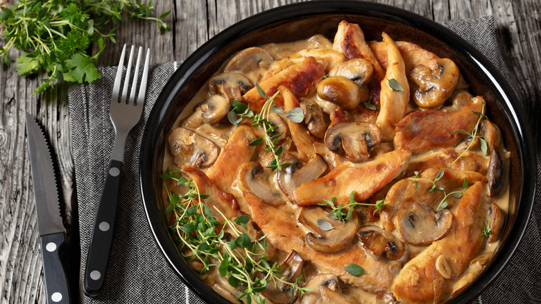 Creamy chicken Stroganoff served in a black bowl with utensils and greenery on the side