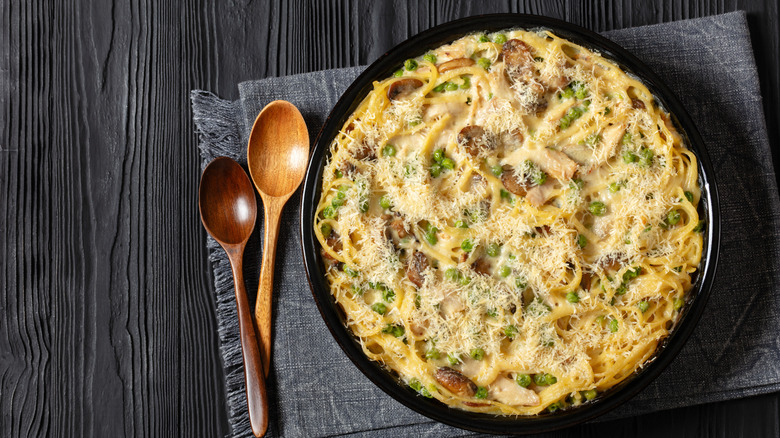 Chicken Tetrazzini on a black table with two wooden serving spoons