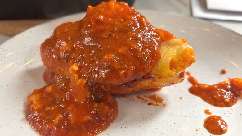 Close-up of stuffed shell covered with meat sauce on white plate