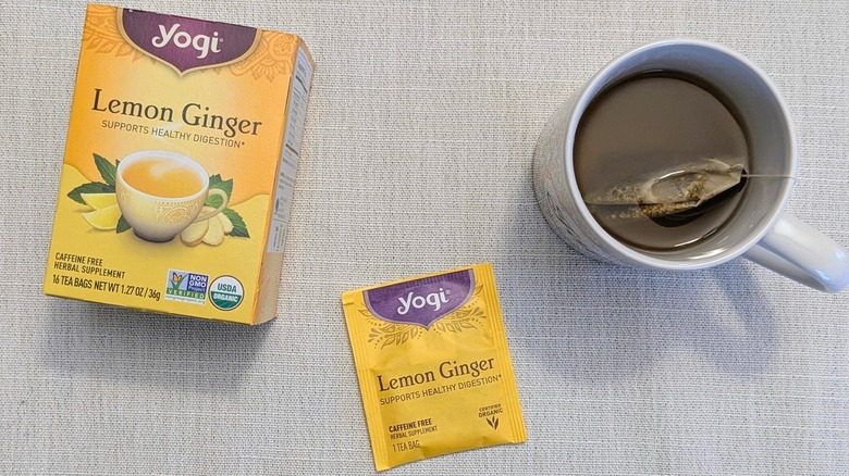A box of lemon Ginger tea, a tea bag, and a mug on a white tablecloth