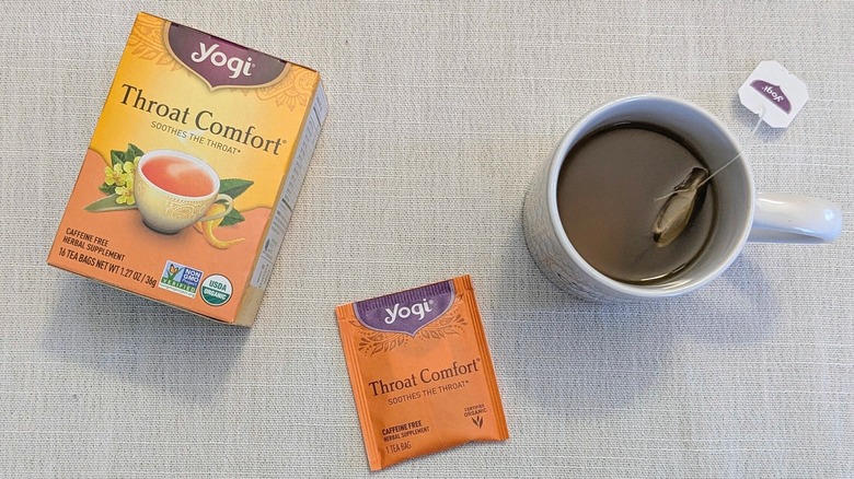 A box of Throat Comfort tea, a tea bag, and a mug on a white tablecloth