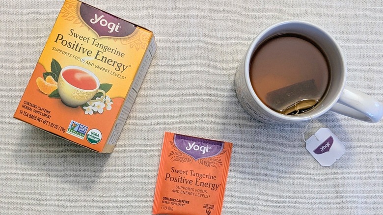 A box of Sweet Tangerine Positive Energy tea, a tea bag, and a mug on a white tablecloth