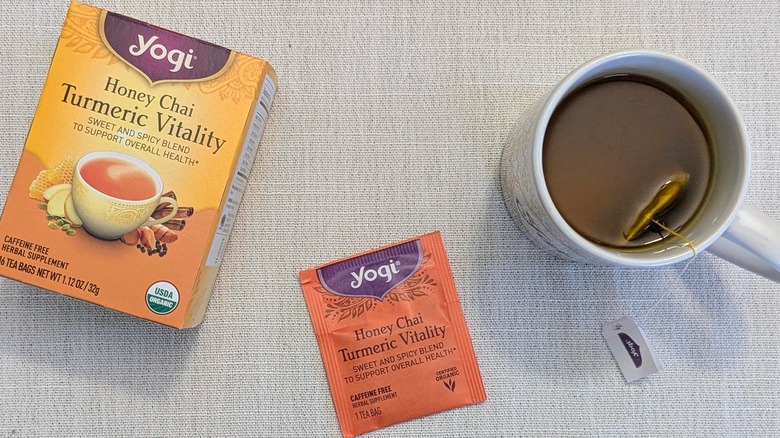 A box of Honey Chai Turmeric Vitality tea, a tea bag, and a mug on a white tablecloth