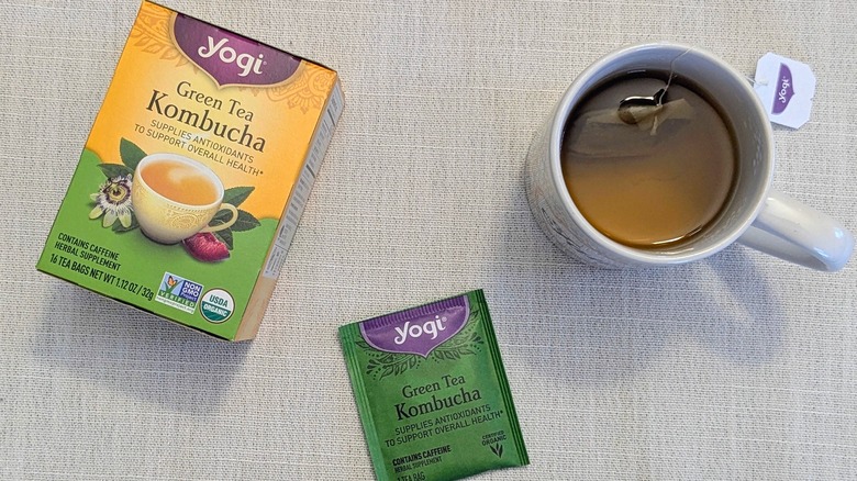 A box of Green Tea Kombucha tea, a tea bag, and a mug on a white tablecloth