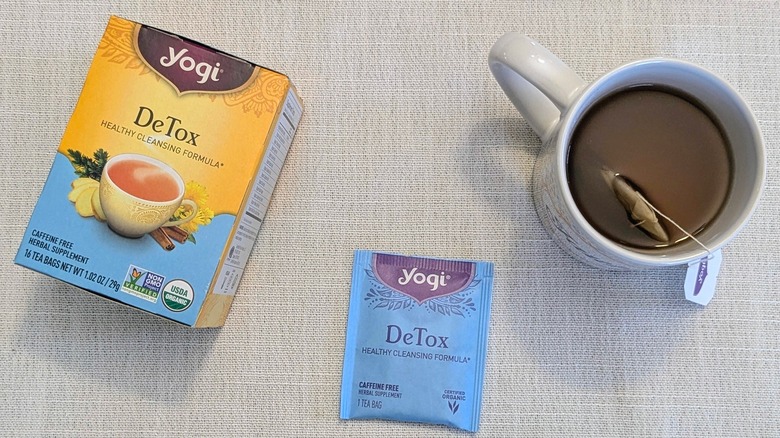 A box of Detox tea, a tea bag, and a mug on a white tablecloth