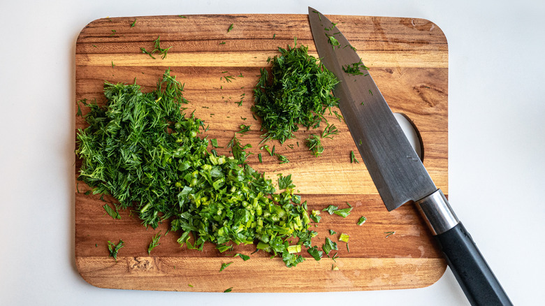 Chopped fresh herbs on wooden cutting board with knife
