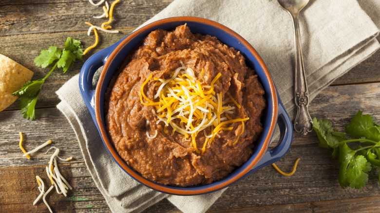 Refried beans in blue and orange dish, topped with shredded cheese