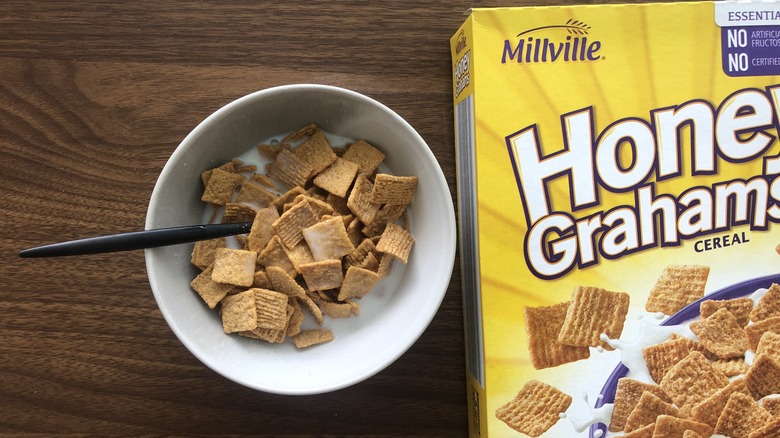 Bowlful of Millville Honey Graham Squares with milk and spoon.