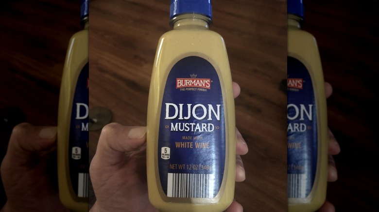 A hand holding a bottle of Burman's Dijon mustard made with white wine