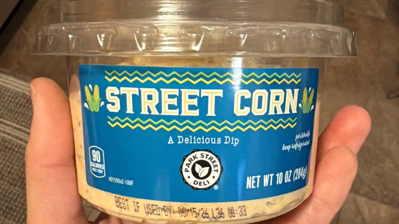 A hand holding a container of Park Street Deli street corn dip