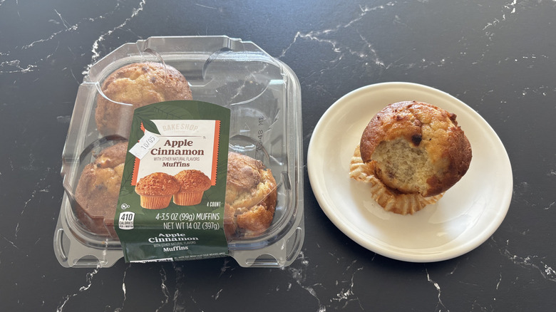 A package of Bake Shop Apple Cinnamon Muffins next to muffin on a white plate