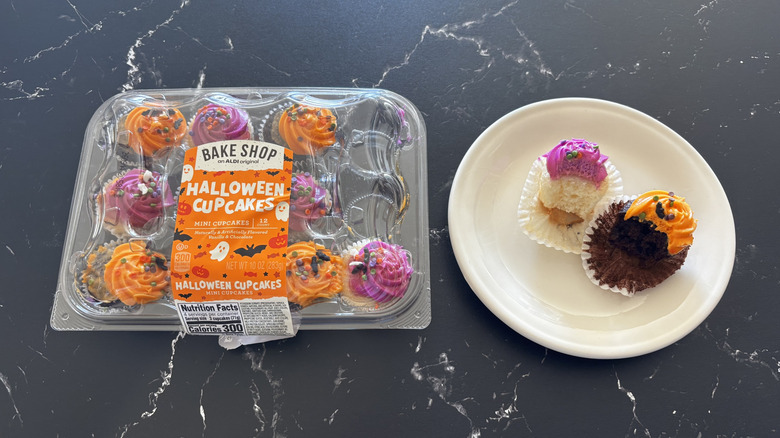 A Bake Shop Halloween Mini Cupcakes container next to two half-bitten mini cupcakes on a white plate