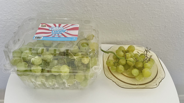 Plastic container of cotton candy grapes with some grapes on a separate plate