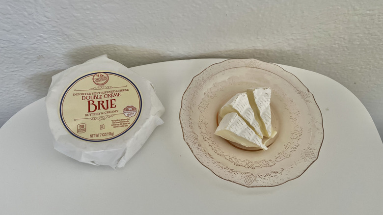 A wheel of brie cheese next to a plate with three slices of brie cheese