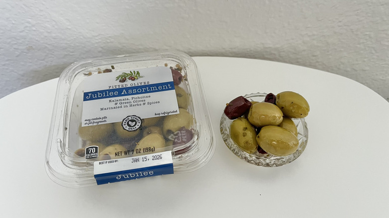 Olive assortment in a original plastic packaging with a few pieces in a glass dish