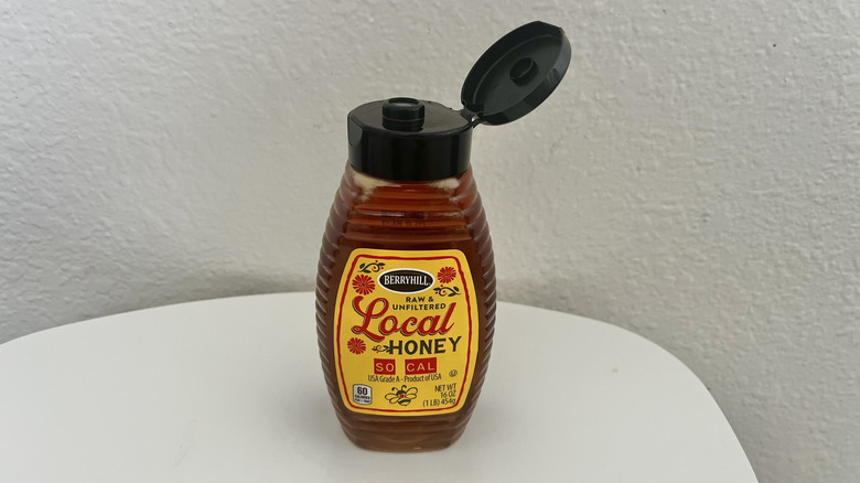 Open squeeze bottle of honey on a white table in front a white background