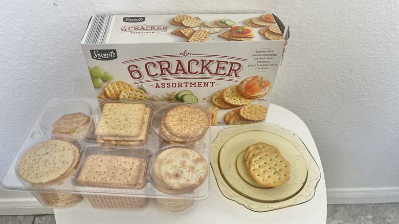 Box and a plastic packaging of assortment of six different types of crackers next to some crackers on the plate