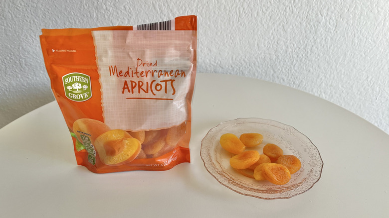 Dried apricots in a bag with some pieces on a glass plate