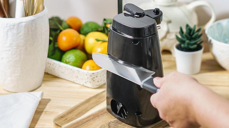 A person using the knife sharpener on the back of a black electric can opener