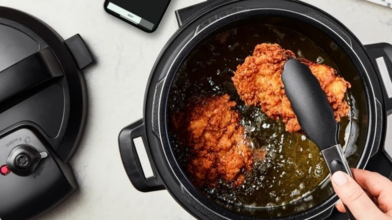 Someone using tongs to take fried chicken out of a pressure cooker