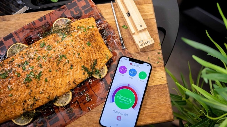 A phone displaying the Meater app sitting on a cutting board next to a grilled salmon fillet