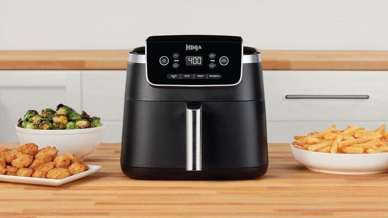 A black Ninja air fryer unit on a wooden table top with dishes next to it